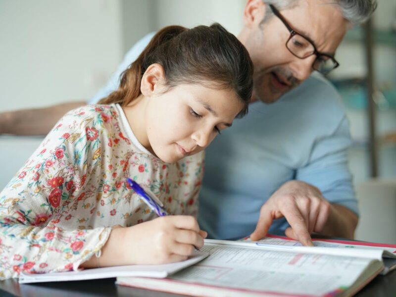دختر در حال مشق نوشتن و راهنمایی پدر